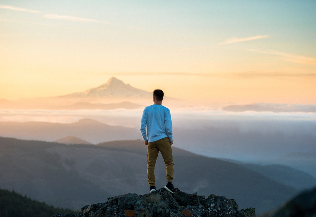 Billede af mand på toppen af et bjerg som kigger ud over horisonten.